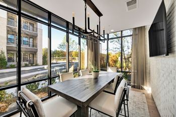 A dining room with a long table and chairs with a view of a street outside.